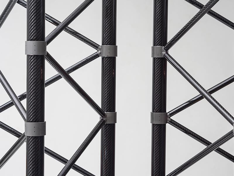 Image shows a details of the two custom truss structures / marine sensor masts placed standing side-by-side in a vertical position. The backgound is white.  The focus is on the connection points where the tubes placed at angles connect to the primary tubes that run the full length of the structure. 